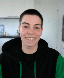 Frau, im grün-schwarzen Hoodie, lächelnd in der Küche