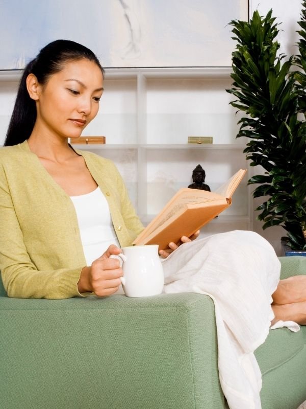 Frau sitzt ruhig mit einem Buch auf dem Sofa